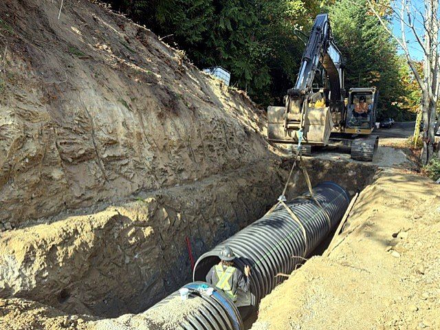 Excavator lowering large corrugated culvert pipe into a deep trench