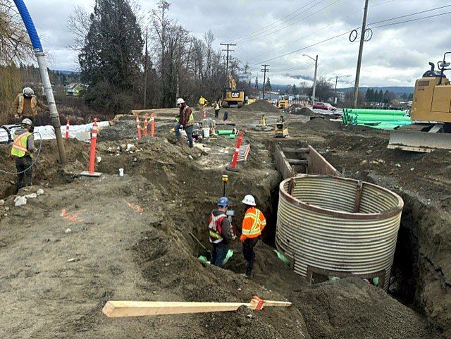 Crew surveying grade beside a CSP manhole