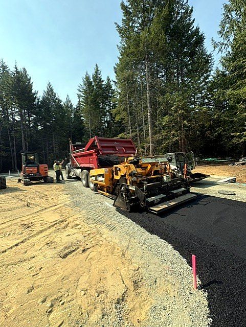 Asphalt paver laying a new road with mini excavator nearby