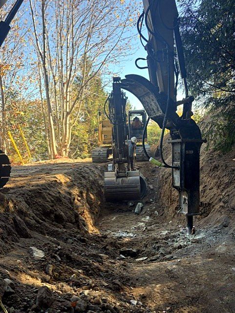 Excavator with hydraulic hammer breaking rock in a trench