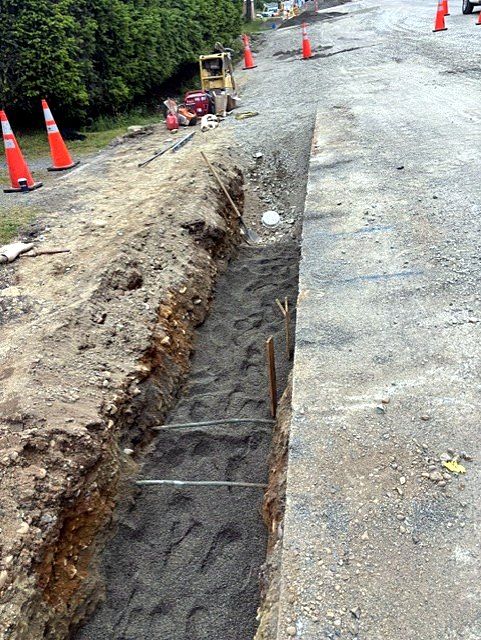 Long utility trench with sand bedding and traffic cones